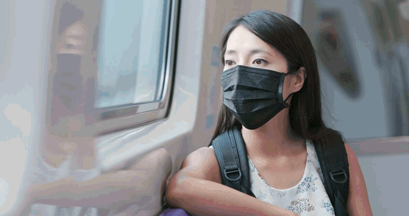 Foto de uma mulher de máscara cirúrgica, sentada próxima a uma janela. Há muito tempo usar máscaras é um dos costumes do Japão.