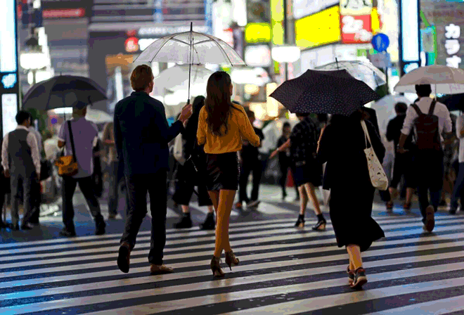 Foto de pessoas atravessando a rua. Muitas delas usam guarda-chuvas, mesmo sem chuva. Mais um dos curiosos costumes da cultura japonesa.