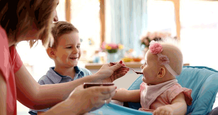 Foto de bebê sendo alimentado por uma mulher. O au pair é um dos tipos de intercâmbio em que é possível trabalhar como babá.