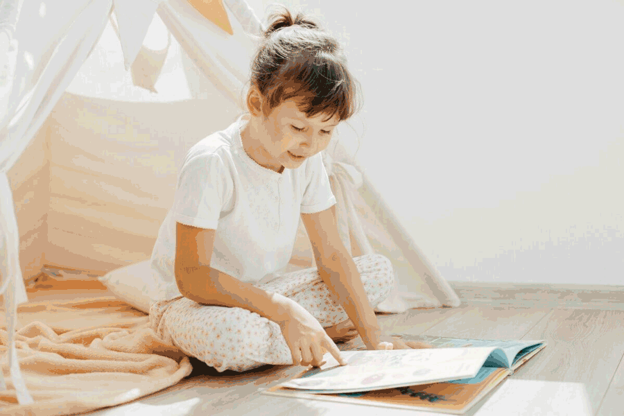 Foto de menina lendo um livro. Há vários métodos para alfabetizar a criança.