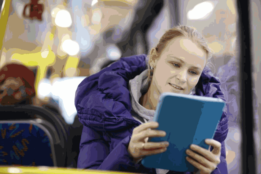 Foto de mulher lendo em tablet no ônibus. Escolher o melhor formato é uma das principais dicas de leitura.