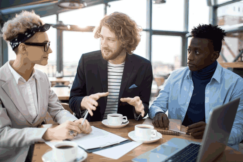  Foto de três pessoas em uma mesa, conversando. Aprender como ser fluente em inglês é muio importante profissionalmente.