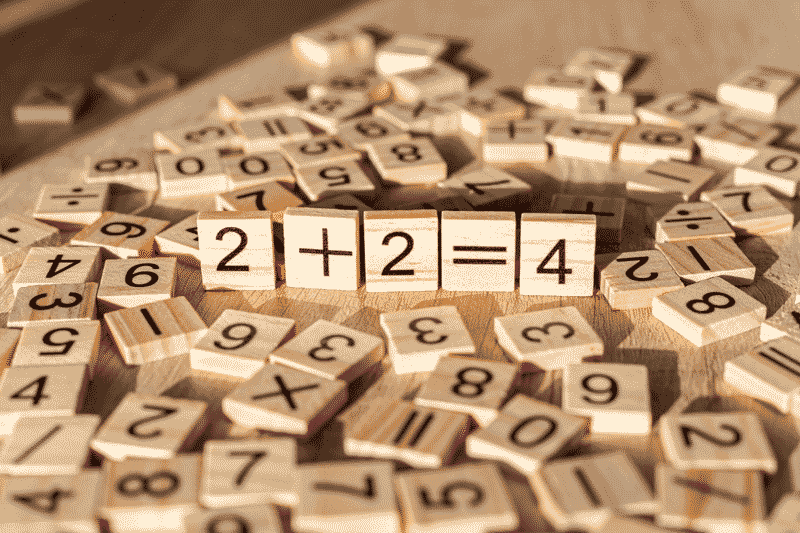 Foto de blocos de madeira representando a conta dois mais dois igual a quatro. O letramento matemático propõe o uso aplicado da matemática.