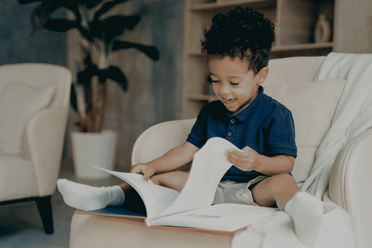Foto de menino sorridente lendo livro. Como ensinar a ler é algo importante para a criança, saiba como fazer.